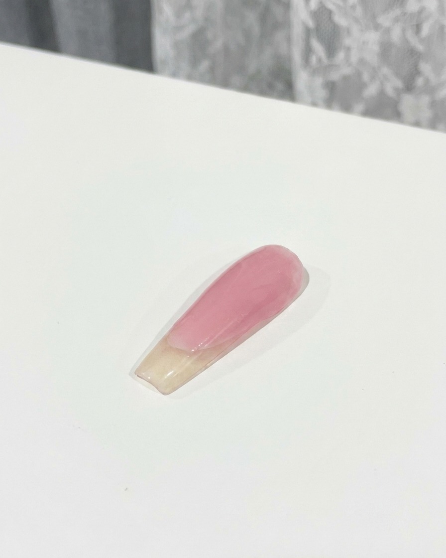Un pinceau appliquant une couche de top coat sur un nœud rose 3D fixé sur un ongle.