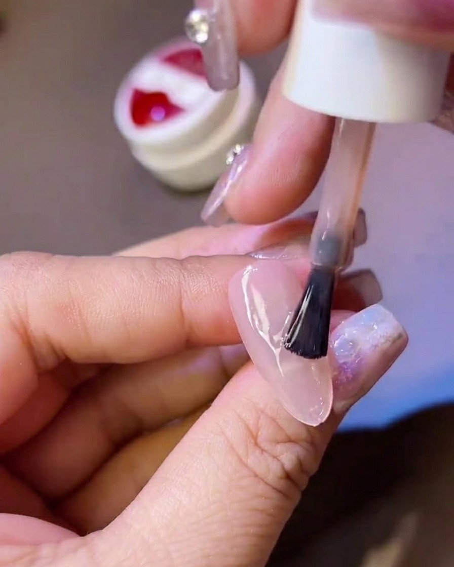 Une main tenant un pinceau de vernis, appliquant une couche de top coat mat sur une capsule dongle translucide.