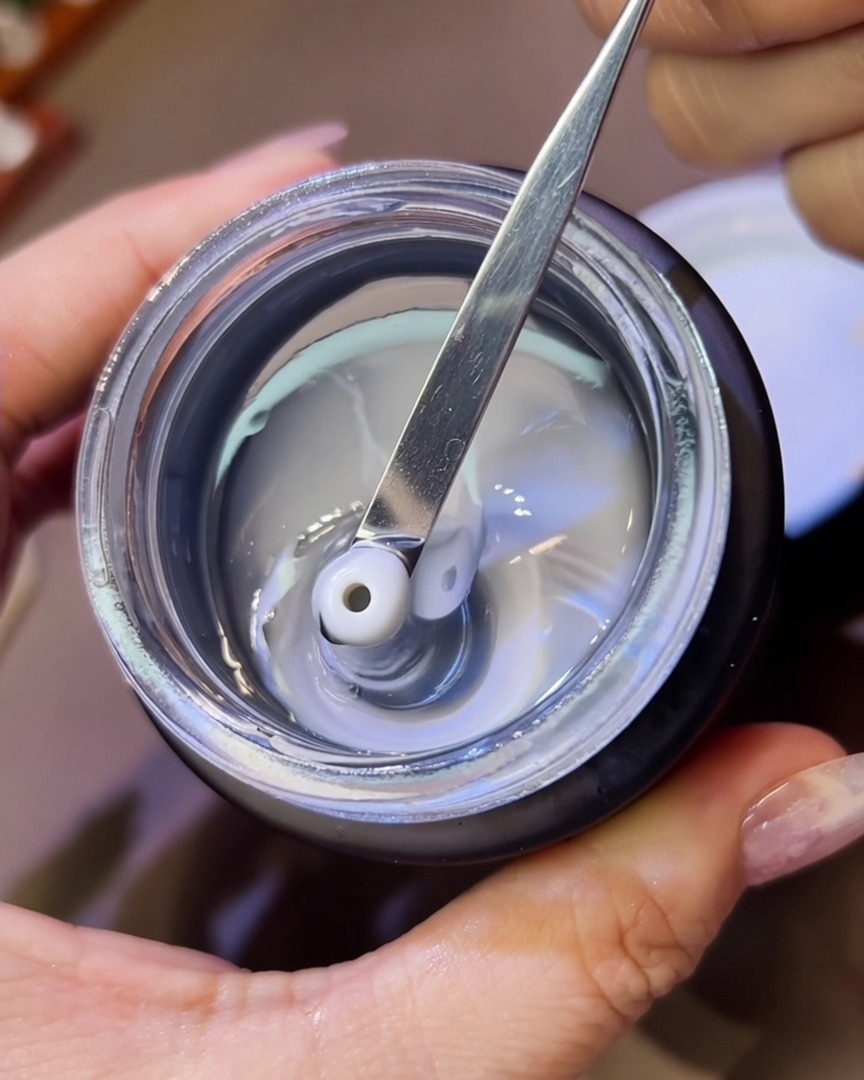 Gros plan sur un outil en métal déposant de petites perles de gel de modelage épais et transparent sur un ongle.