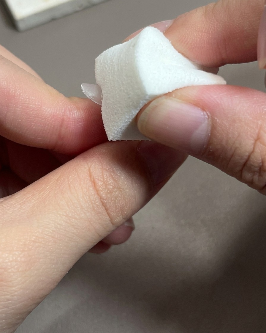 Gros plan sur un pinceau appliquant un vernis gel rose transparent sur une capsule dongle.