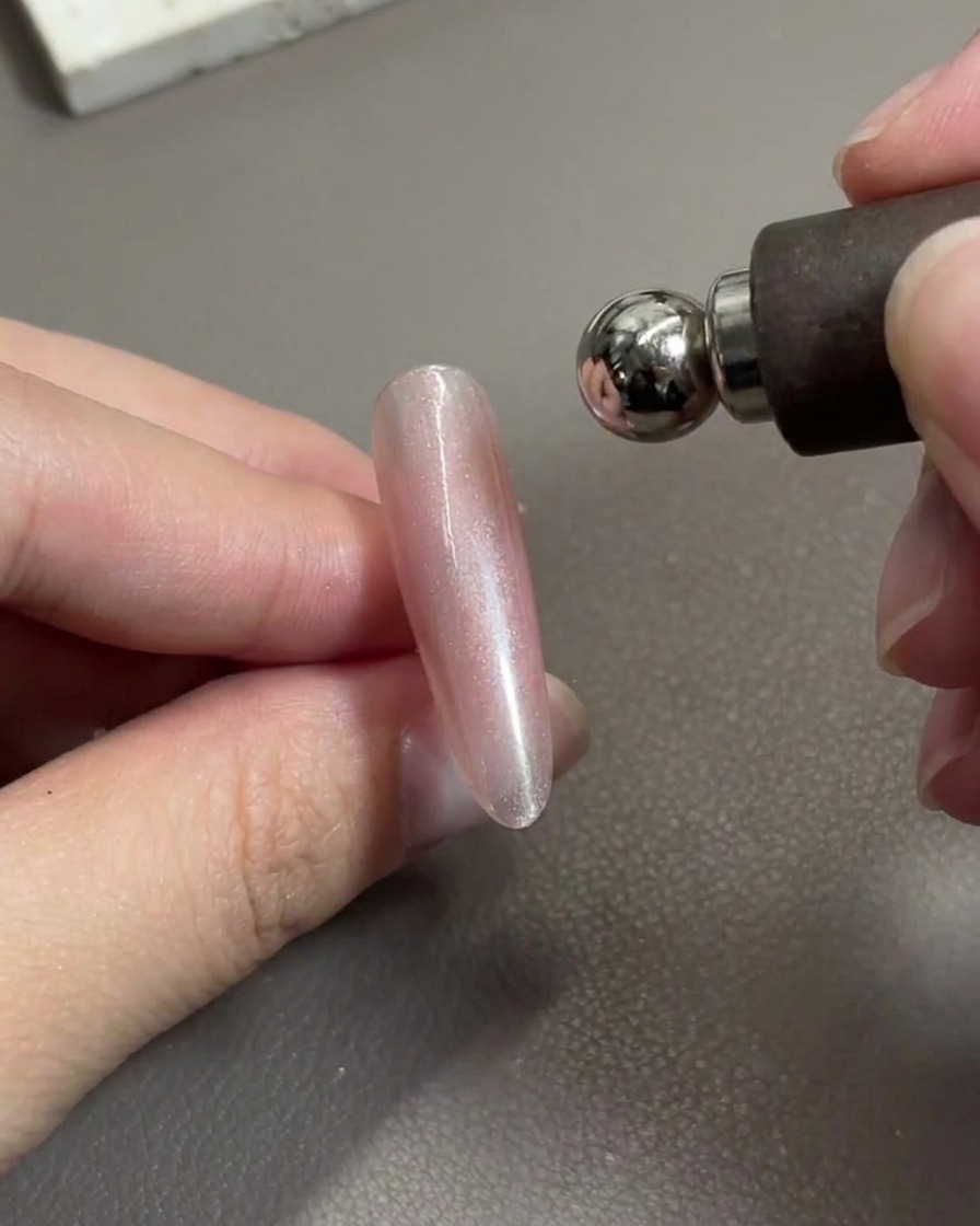 Un outil magnétique positionné au-dessus dun ongle en gel rose brillant, déplaçant activement les particules métalliques.