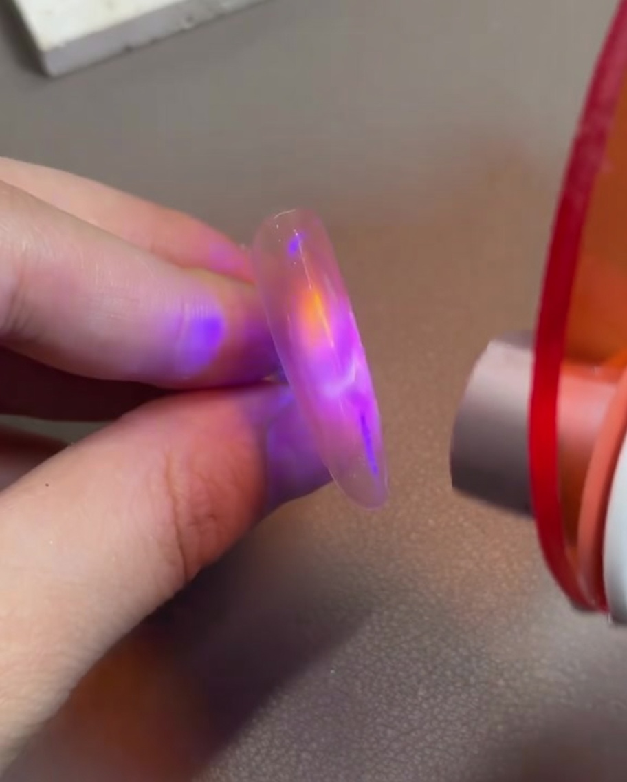 Un doigt avec du gel œil de chat rose tenu sous une petite lampe de catalyse LED portative pour fixer le design magnétique.