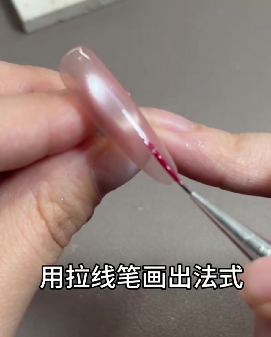 Un pinceau fin pour nail art dessinant une ligne rose rouge délicate le long du bord libre de longle.