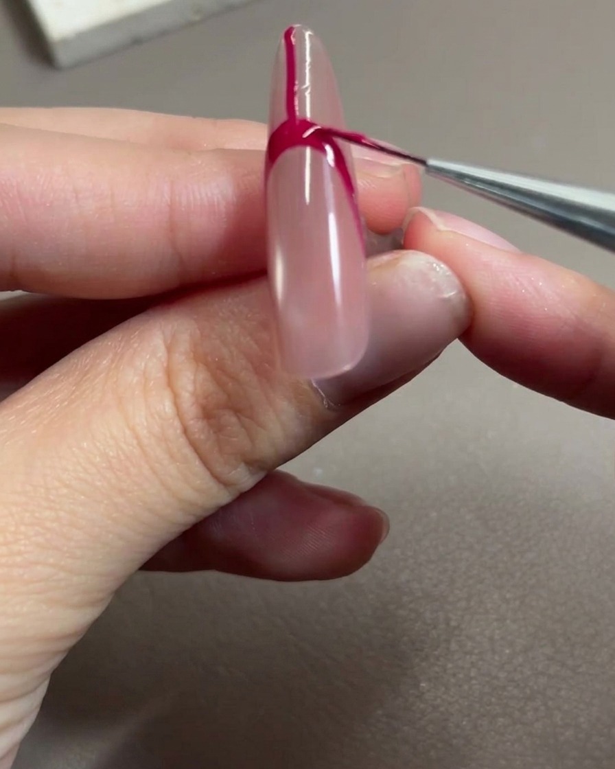 Un pinceau nail art appliquant du gel rose rouge pour remplir lespace à lintérieur du contour de la French.