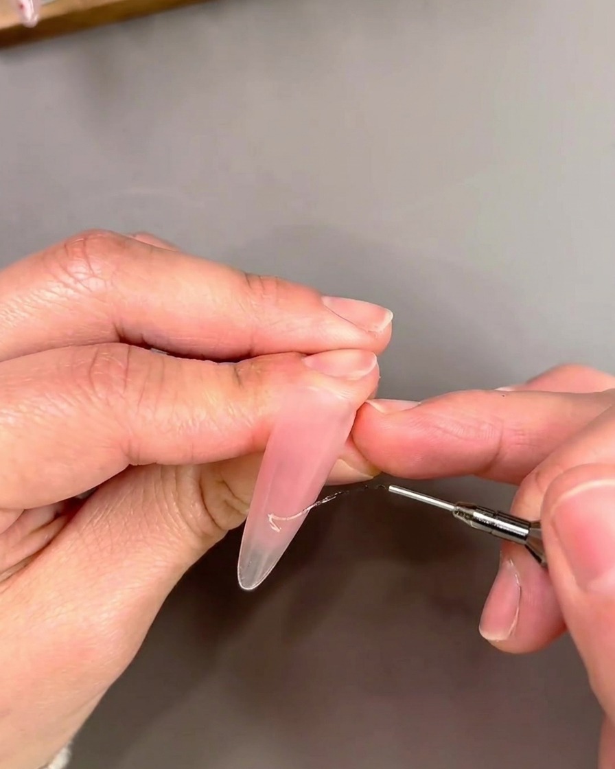 Gros plan dun pinceau liner appliquant du gel œil-de-chat doré dans un design de pointe French.