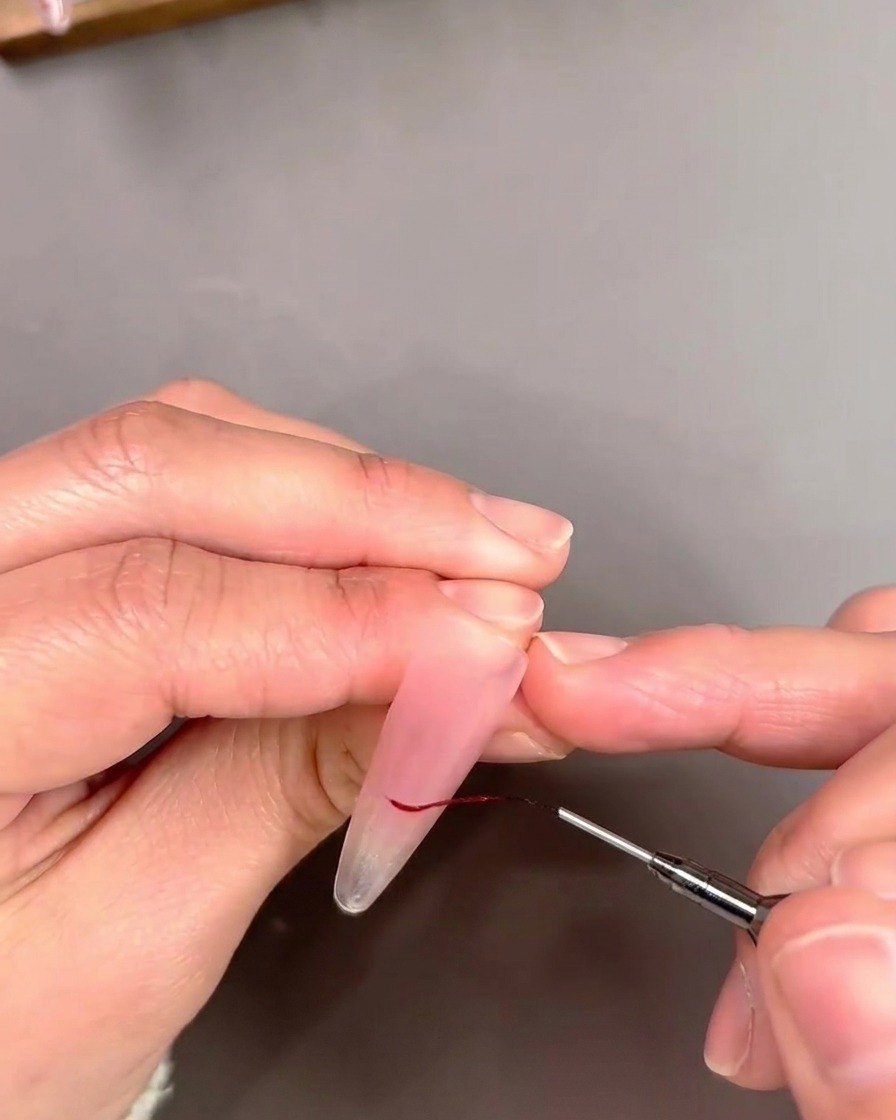 Gros plan dun pinceau liner détourant une pointe French avec une fine ligne de vernis gel rouge.