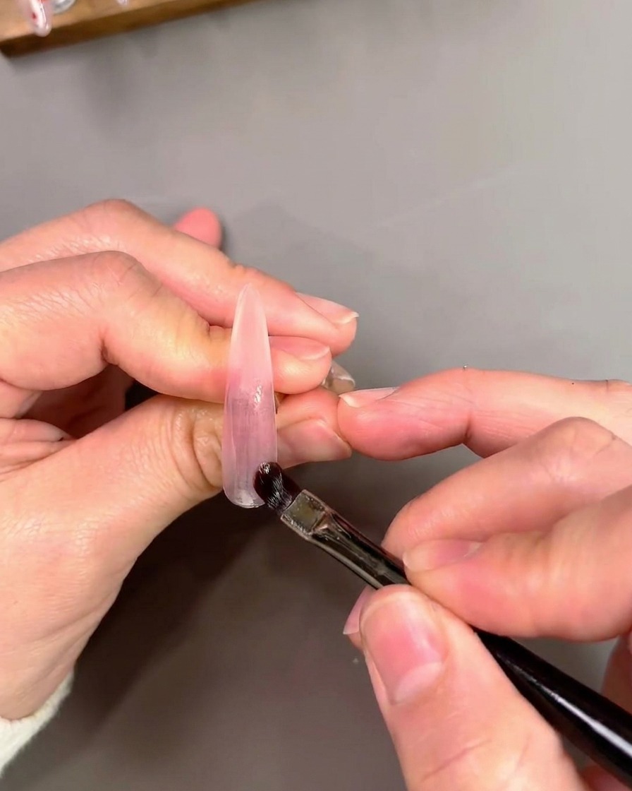 Un pinceau à gel plat appliquant et mélangeant du vernis gel œil-de-chat violet sur un embout dongle artificiel.