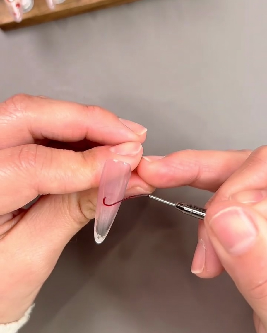 Un pinceau liner fin dessinant une fine ligne courbe en gel rouge près du bord libre dun ongle pour détourer une pointe French.