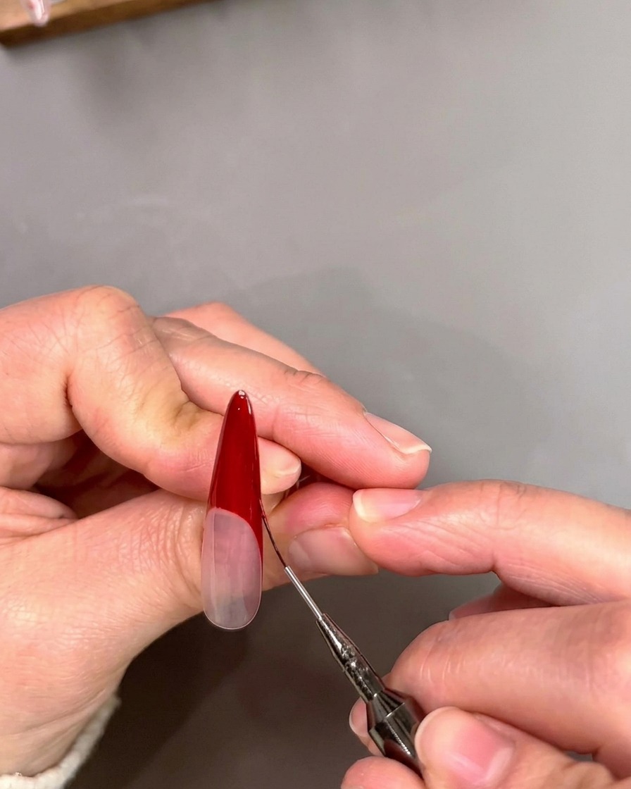 Un pinceau liner fin affûtant le bord intérieur dune pointe French rouge en forme de V profond sur un ongle.