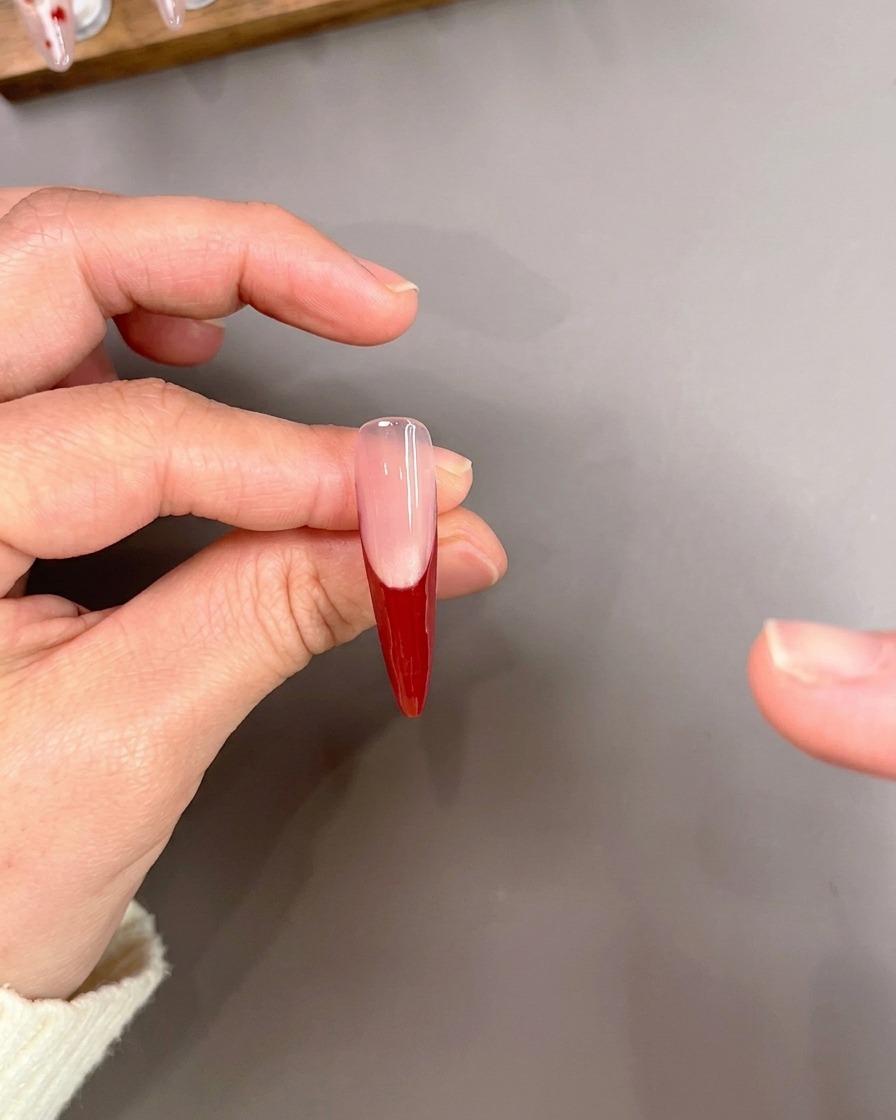 Un pinceau liner dessinant soigneusement de fines lignes rouges sur une pointe dongle avec une base de manucure French rouge.