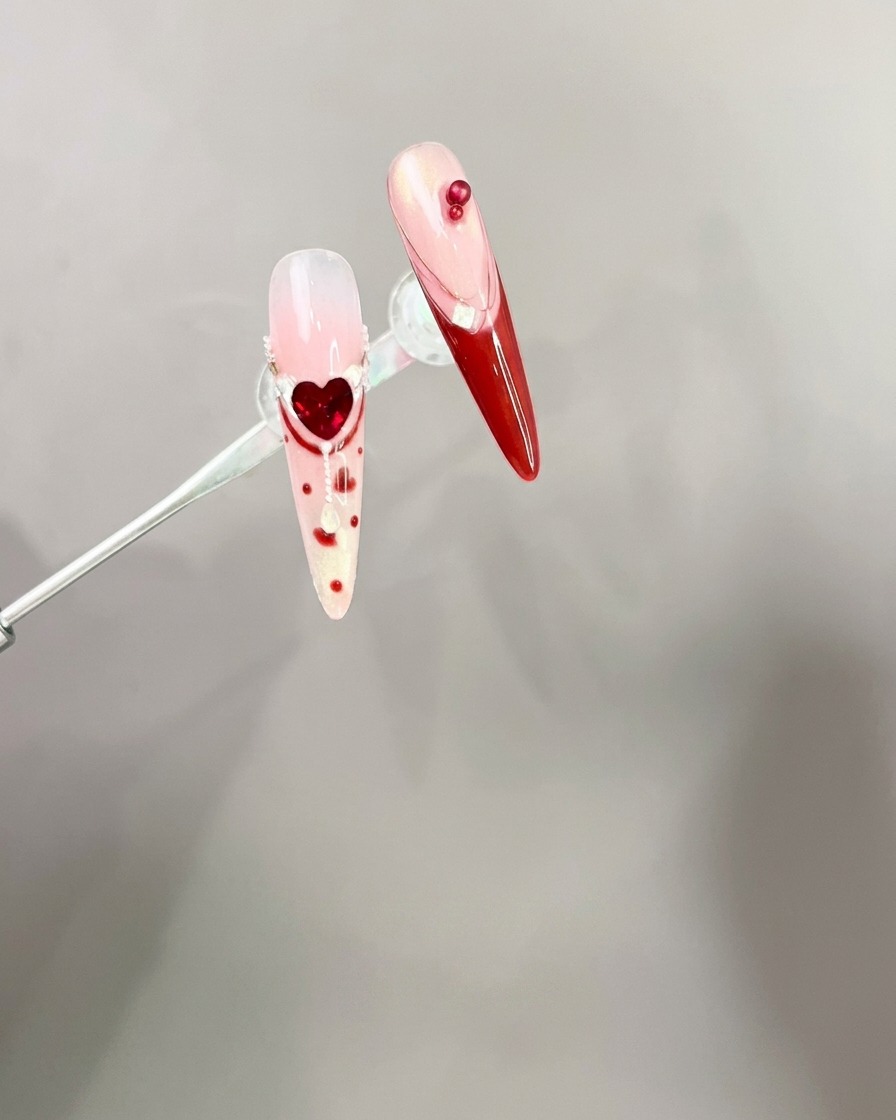 Une pince à épiler plaçant une breloque nœud rouge 3D sur une pointe dongle manucurée.
