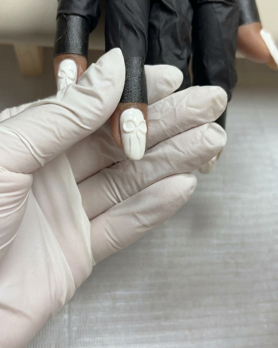 Une vue de dessus dun design de nœud en gel 3D terminé sur un ongle blanc, maintenu stable avant la catalysation finale.