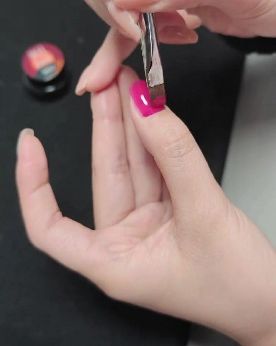 Un pinceau appliquant une deuxième couche de vernis gel magenta sur la couche précédemment catalysée.