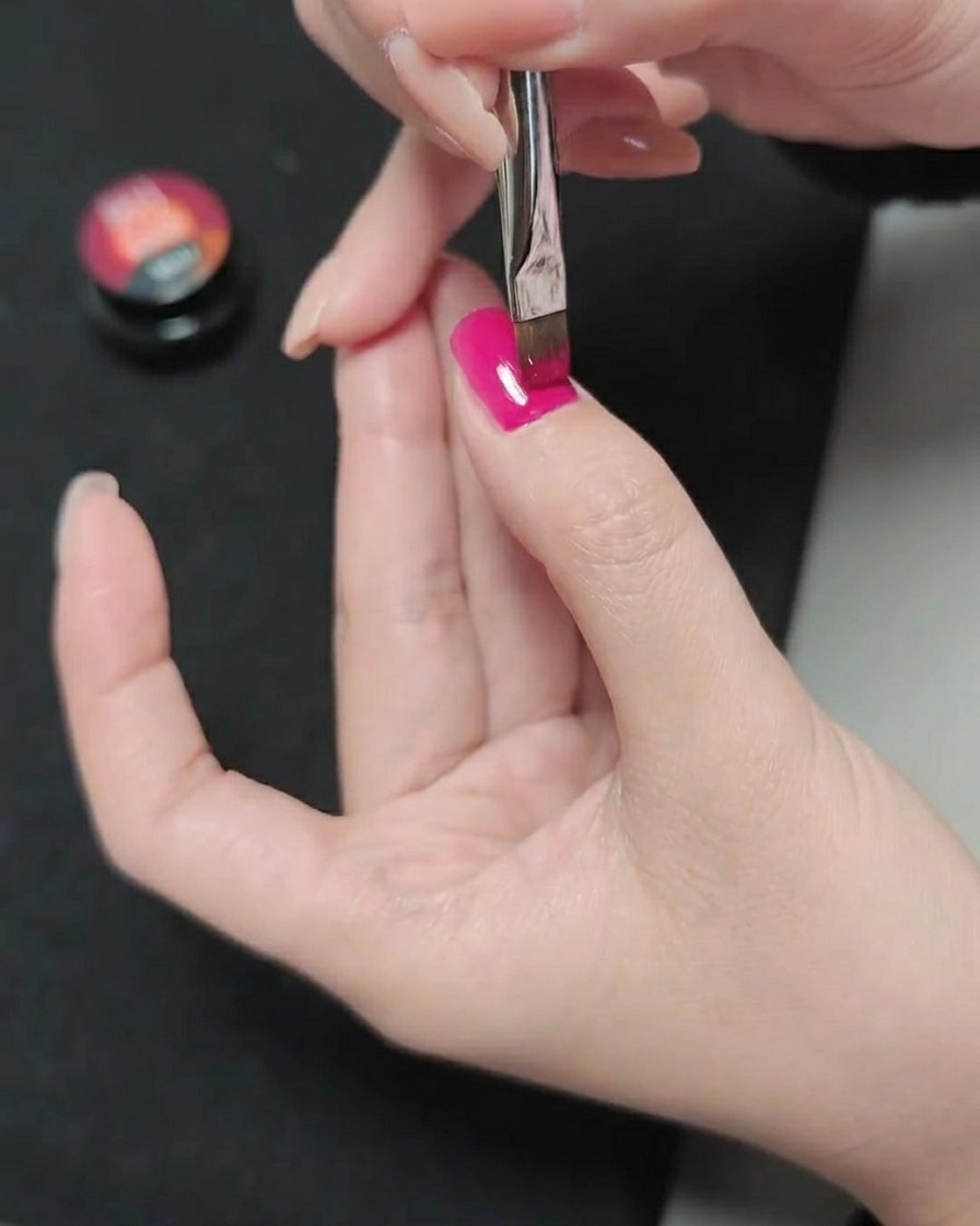 Un pinceau appliquant une troisième couche de vernis gel magenta, créant une finition de couleur lisse et saturée.
