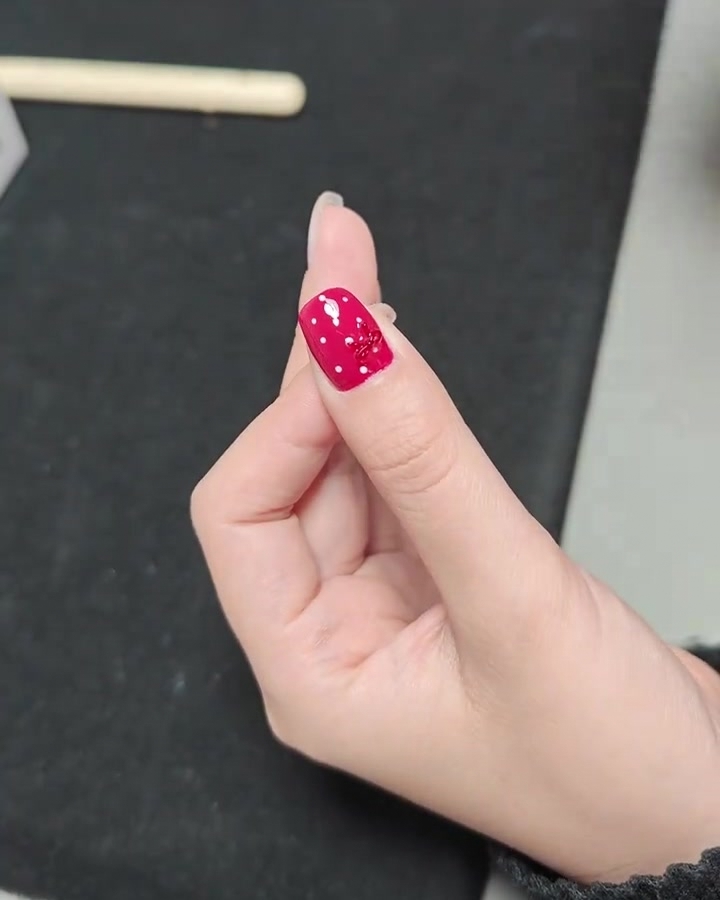 Gros plan dune main avec un ongle à pois et nœud fini à lintérieur dune lampe à ongles UV professionnelle.