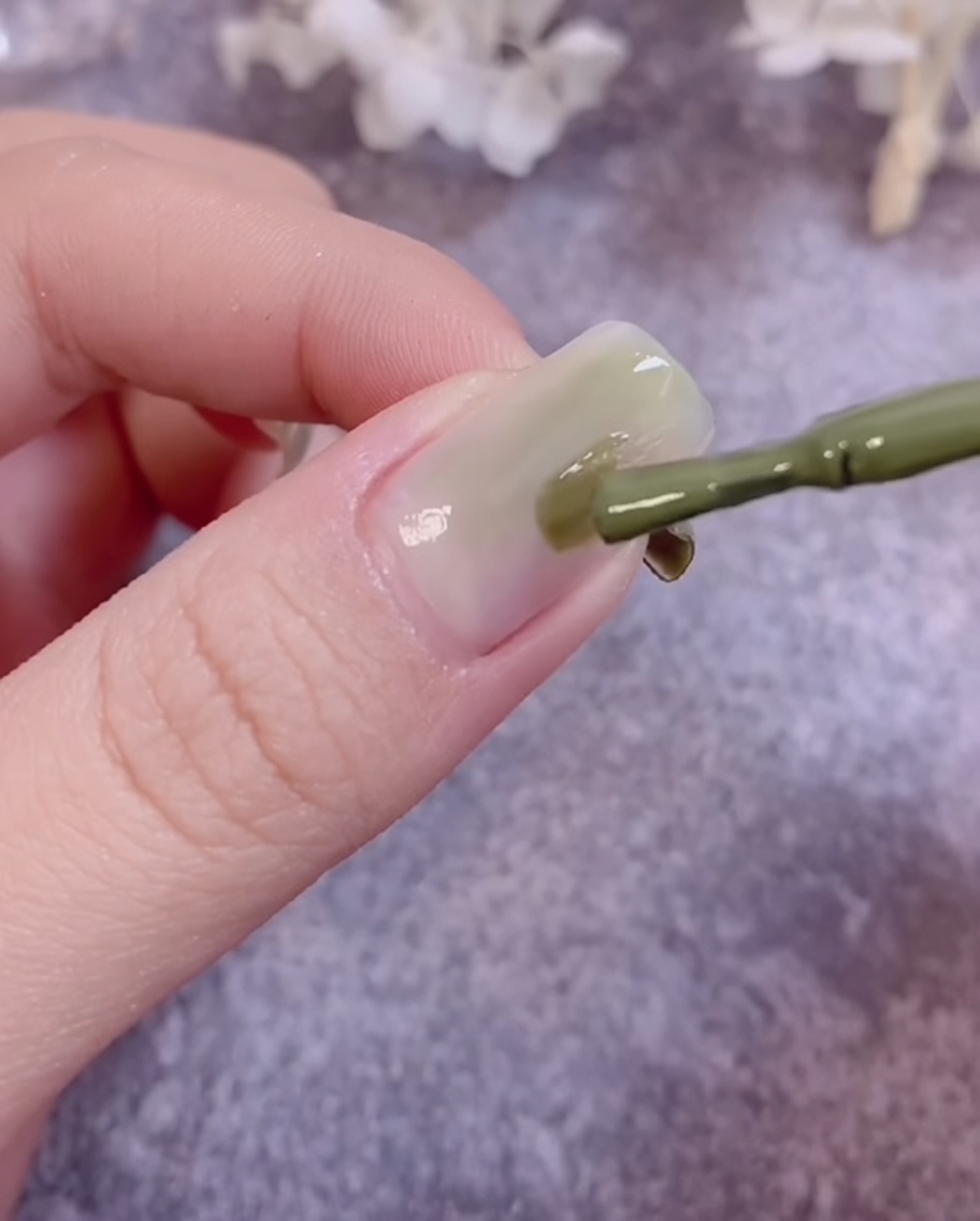 Un pinceau mélangeant du vernis gel vert sur la surface dun ongle pour créer un effet dégradé.