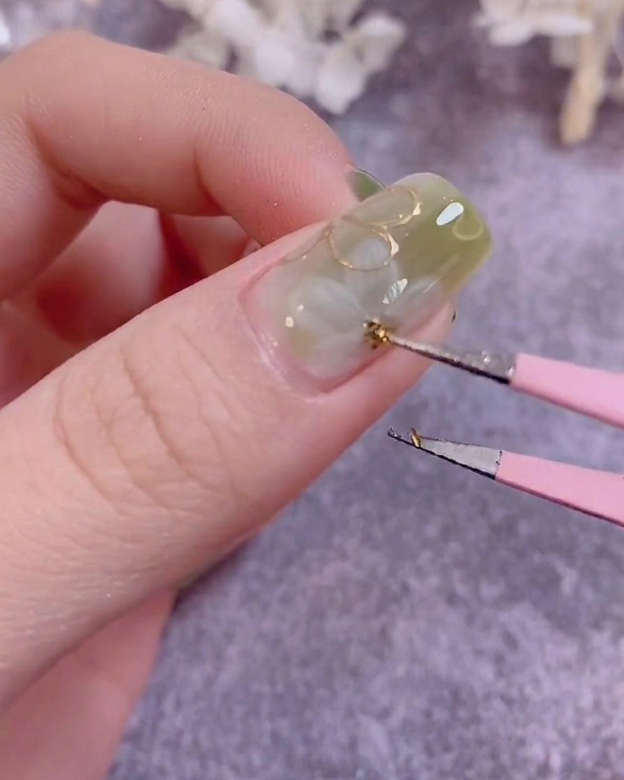 Un pinceau de détail peignant de petites feuilles vertes sur la surface dun ongle manucuré.