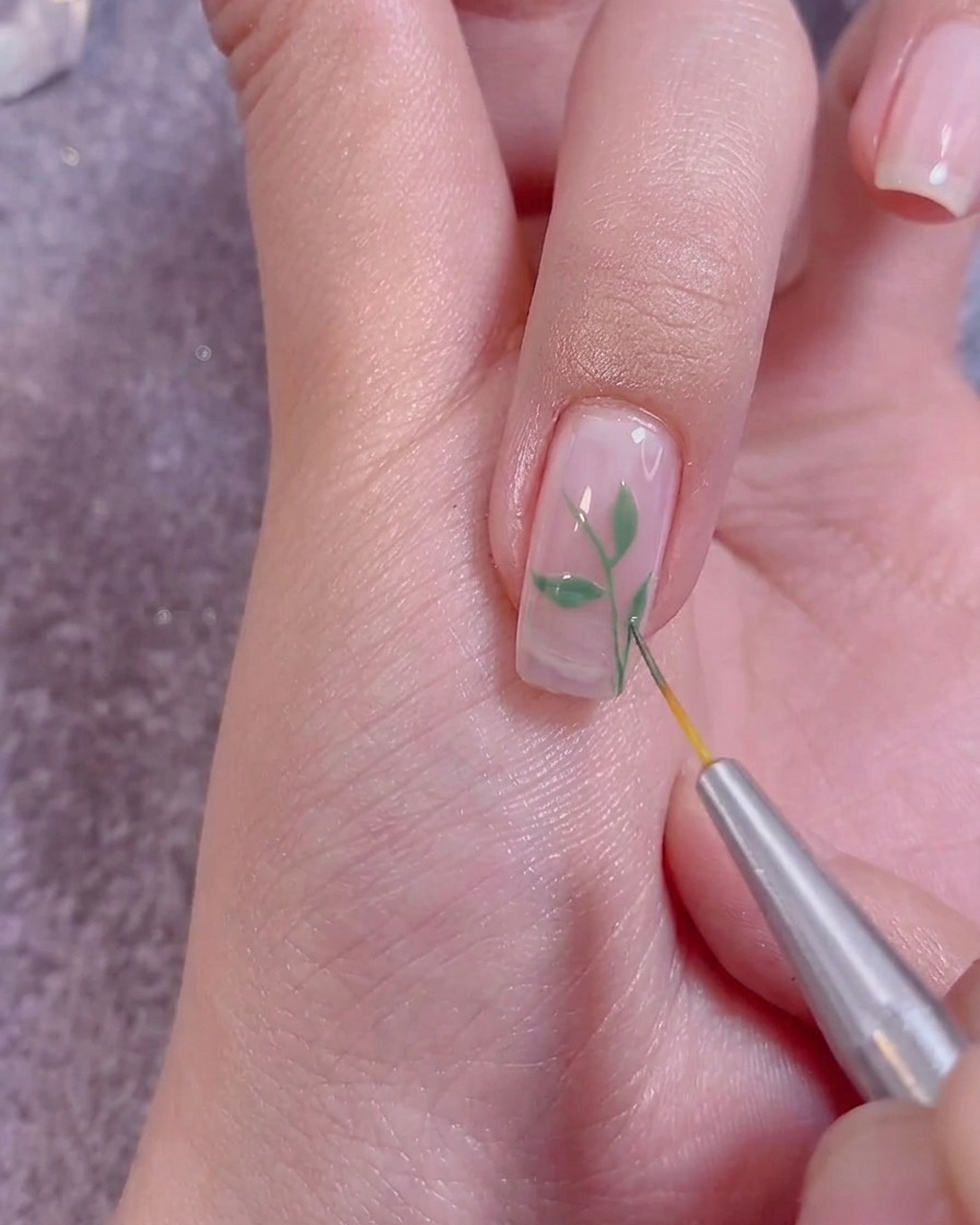 Application dun top coat transparent sur un nail art fini avec un pinceau professionnel.