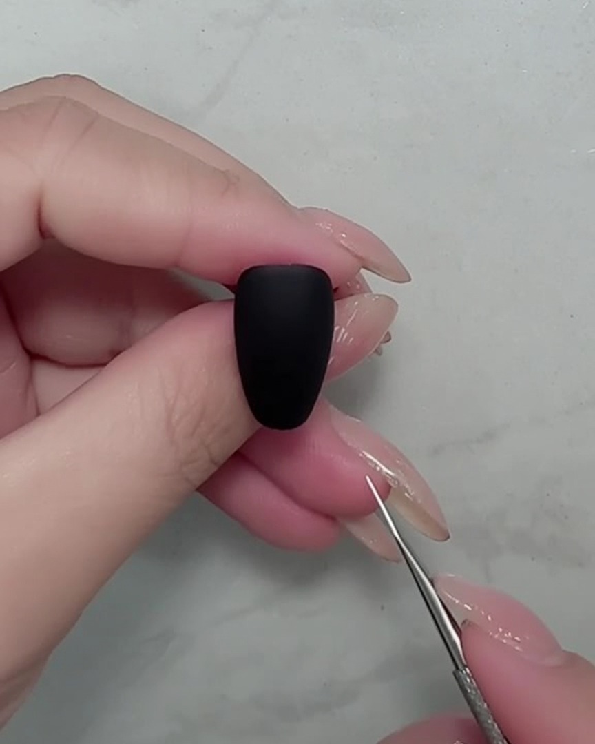 Gros plan sur un pinceau liner traçant de fines tiges blanches sur un ongle noir mat.
