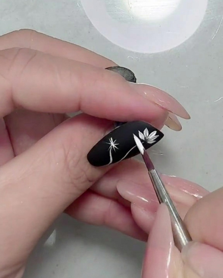 Gros plan dune marguerite blanche parfaitement formée sur un ongle noir mat.