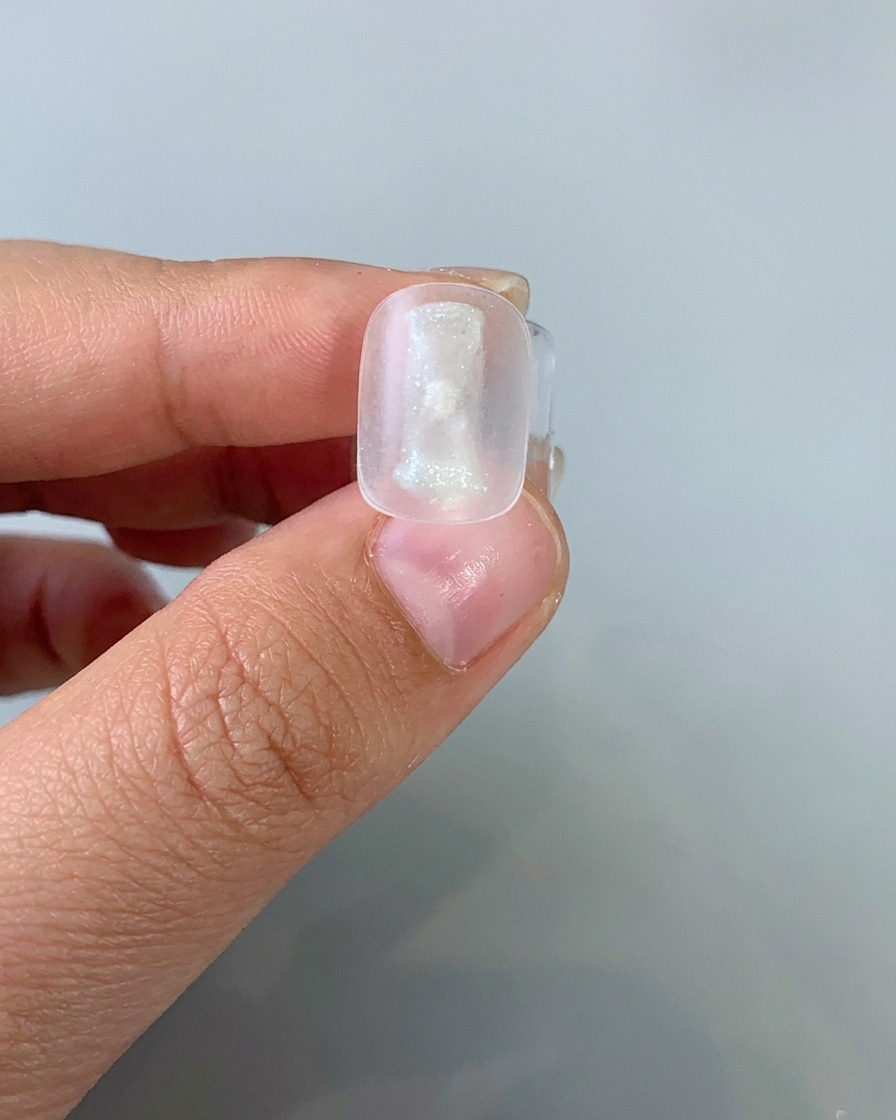 Un pinceau appliquant une fine couche de gel œil-de-chat clair sur une capsule.