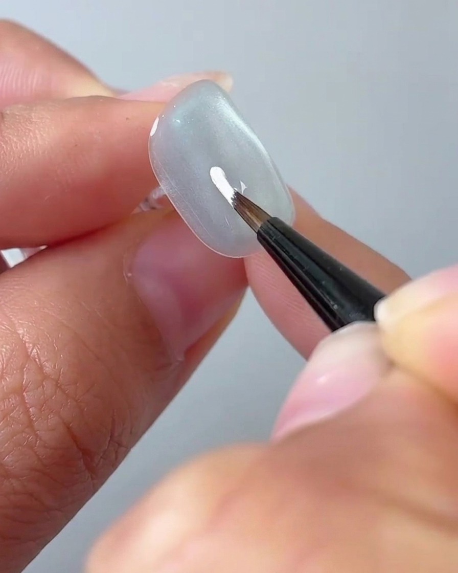 Un pinceau liner fin dessinant un pétale blanc sur une surface dongle gris clair.