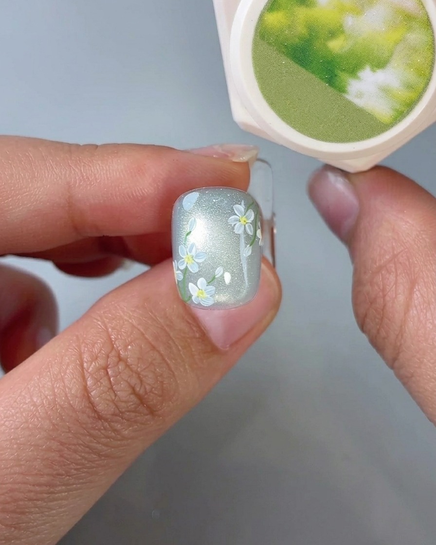 Gros plan dun pinceau appliquant de petits détails de feuilles vertes sur un nail art marguerite.