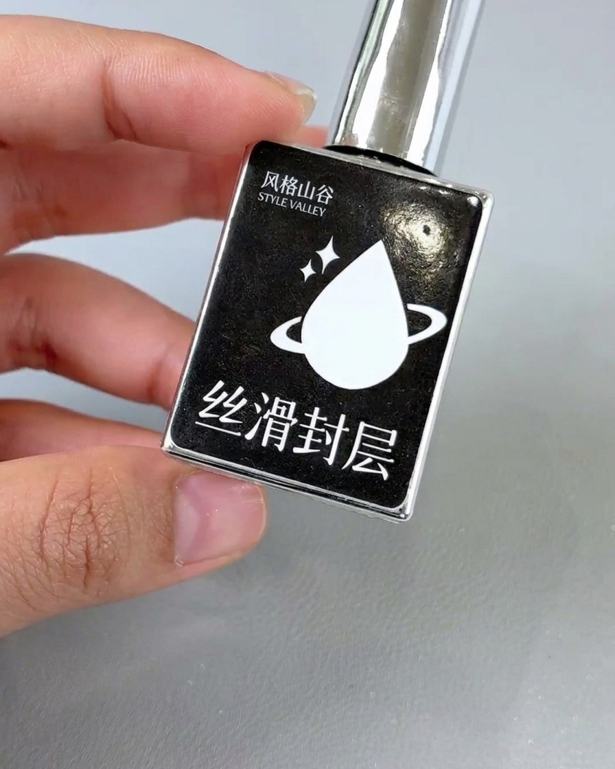 Un pinceau appliquant une couche de finition brillante sur le nail art floral terminé.