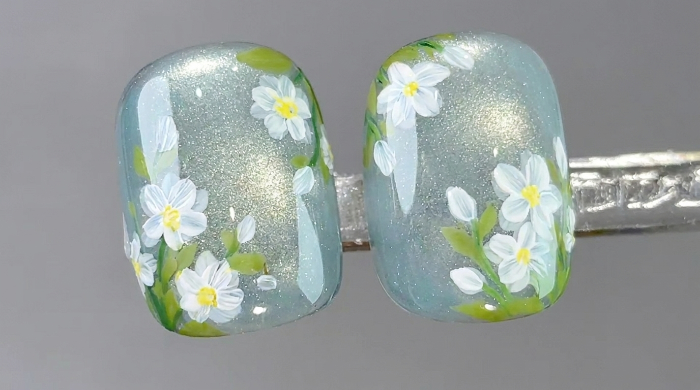 Gros plan détaillé dongles en gel effet œil-de-chat ornés de marguerites peintes à la main et de feuillage délicat.