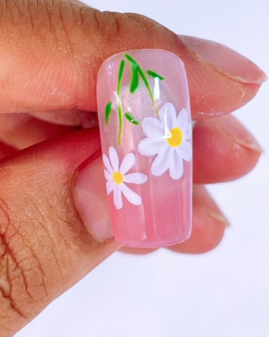 Gros plan dun ongle rose dégradé sur lequel une deuxième petite marguerite est peinte avec du gel blanc et un pinceau liner.