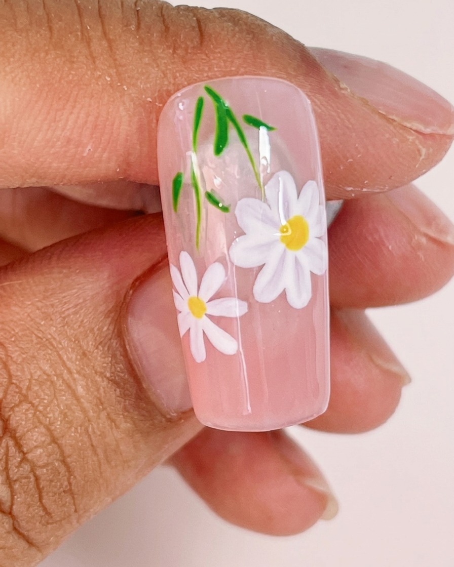 Gros plan montrant un pinceau liner ajoutant de fines tiges vertes et de petites feuilles au design floral.