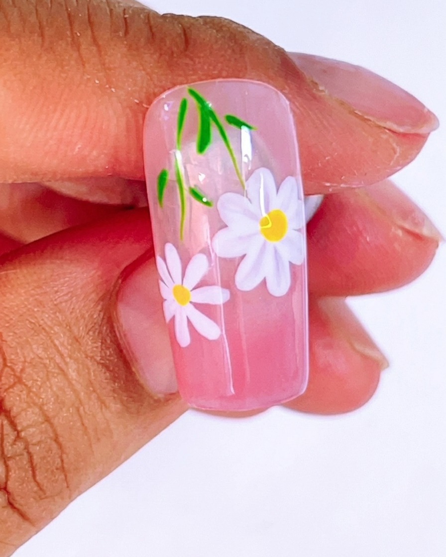 Un pinceau appliquant une couche épaisse et brillante de top coat sur le design de marguerites et feuilles.