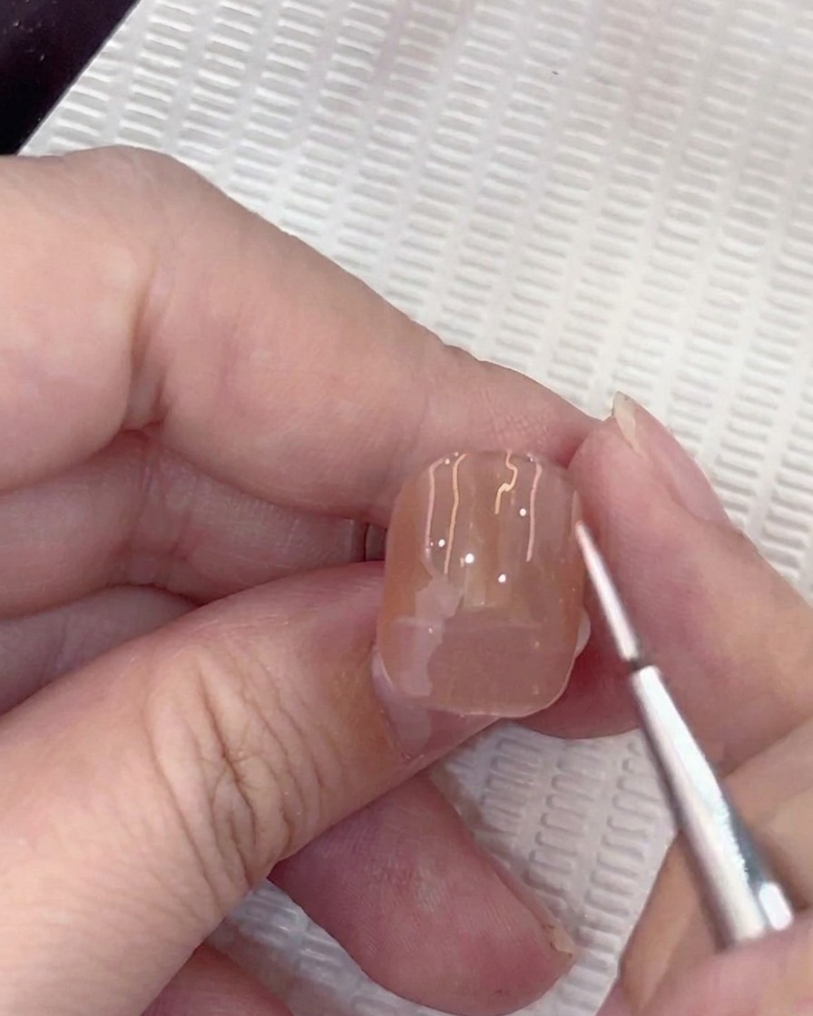 Gros plan dun pinceau liner appliquant un petit point guide blanc au centre dun ongle en gel nude.