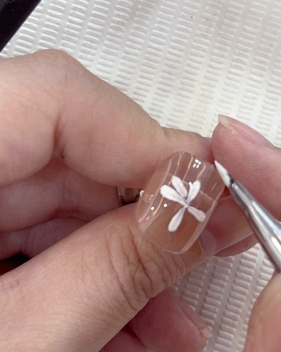 Gros plan dun design de nail art marguerite blanche où un septième pétale est soigneusement placé par un pinceau rond.