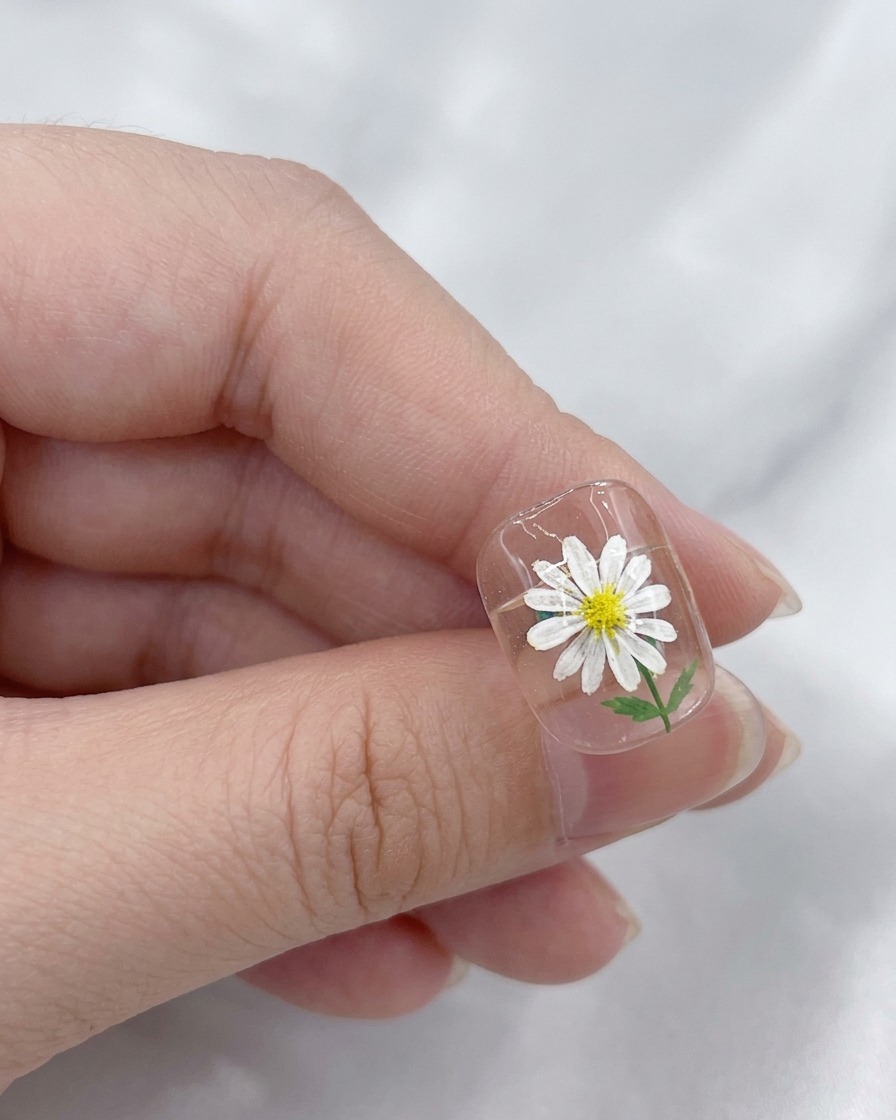 Un pinceau appliquant une couche de finition claire et brillante sur un design de nail art marguerite terminé.