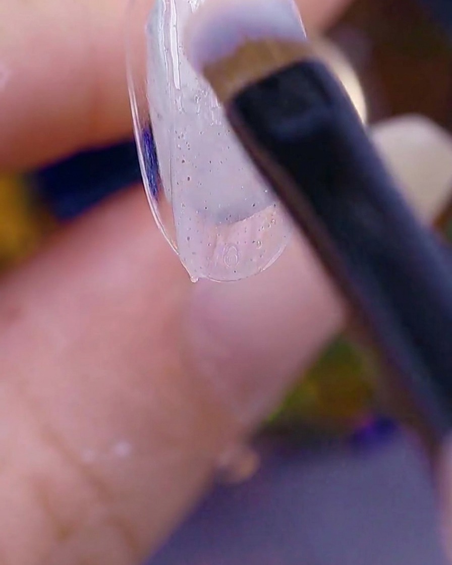 Gros plan dun pinceau appliquant un gel texturé sucre translucide sur le bout dun ongle naturel.
