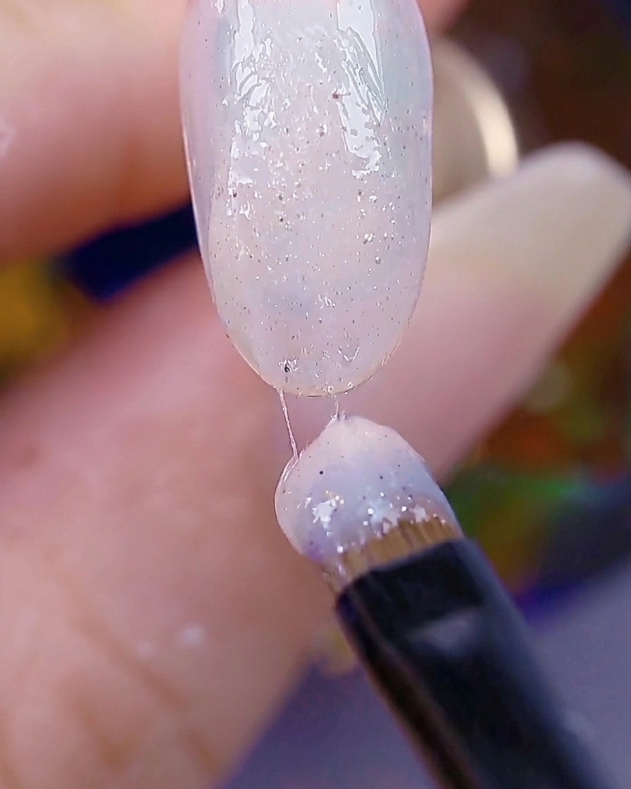 Un pinceau à ongles appliquant une seconde couche de sugar gel, la surface de longle paraissant texturée.