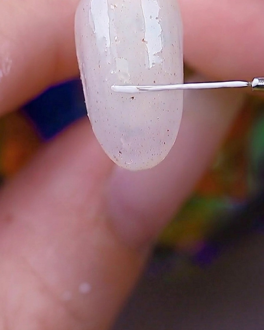 Détail dun pinceau liner traçant un cadre rectangulaire blanc dans le coin dun ongle texturé.