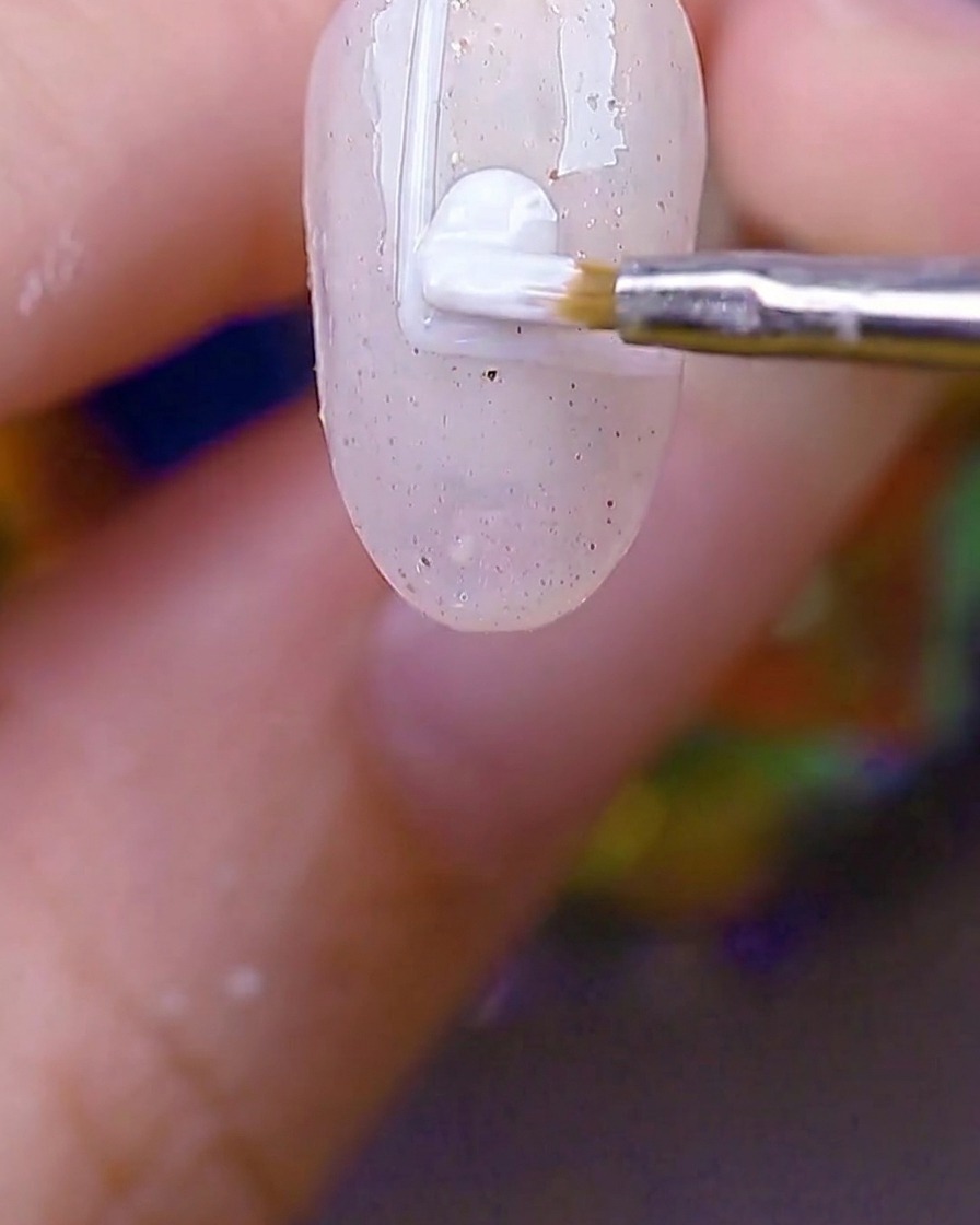 Un petit pinceau rond remplissant le rectangle bordé de blanc avec du gel blanc opaque.