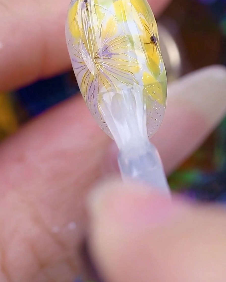 Un pinceau appliquant un top coat transparent brillant sur le nail art terminé.