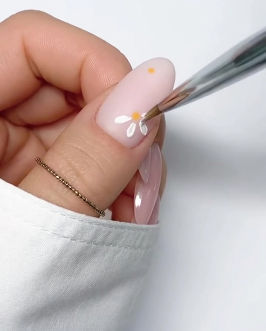 Une marguerite blanche terminée avec cœur jaune sur ongle nude.