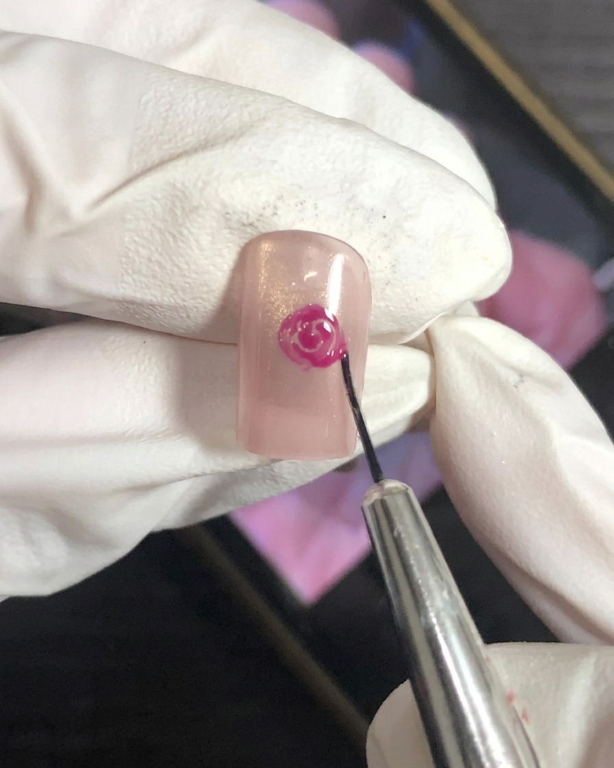 Gros plan dun pinceau de nail art estompant les bords extérieurs dun motif de rose magenta sur une base nude.