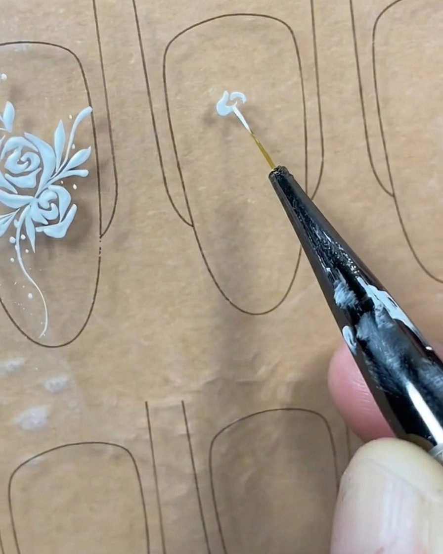 Gros plan dun pinceau liner appliquant un petit point de gel blanc au centre dune capsule transparente.