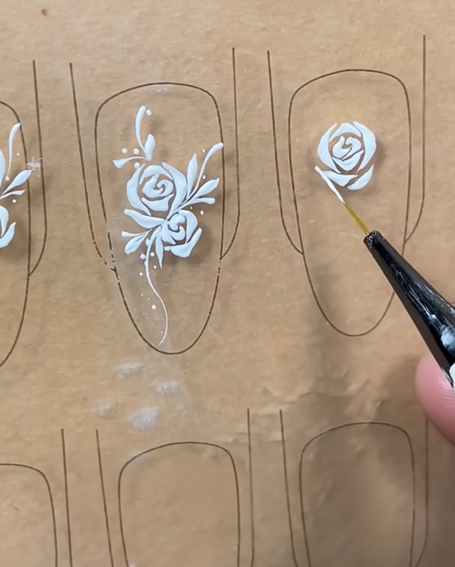 Gros plan dun pinceau liner ajoutant des détails blancs fins sur les pétales extérieurs dun design de rose sur une capsule.