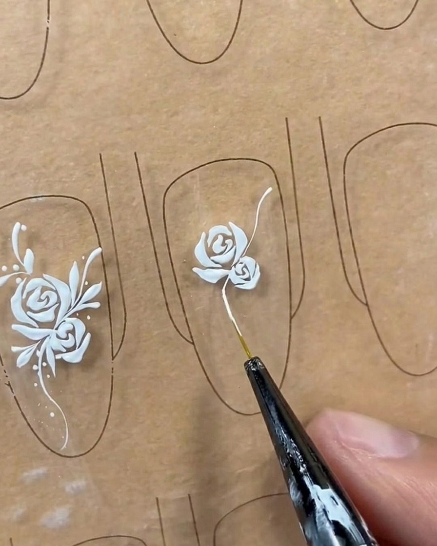 Une longue ligne de tige blanche et fluide tracée depuis la base dun design de rose sur une capsule avec un pinceau liner.