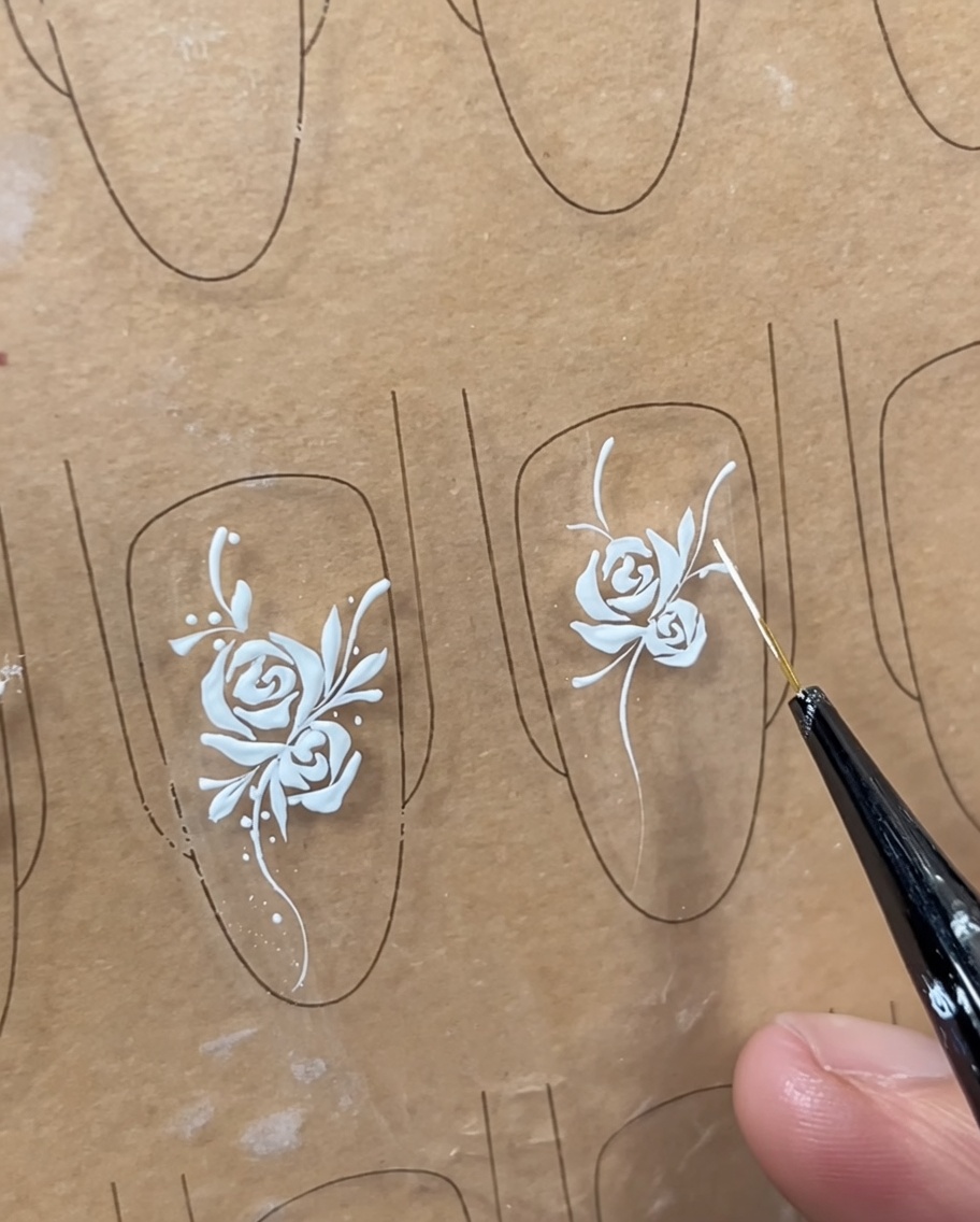 Gros plan dune rose blanche peinte sur un ongle, avec des traits de lumière ajoutés près du centre.