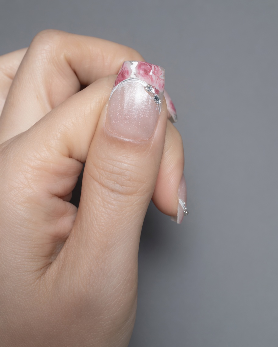 Des ciseaux de précision découpant un motif floral sur une feuille de transfert transparente.