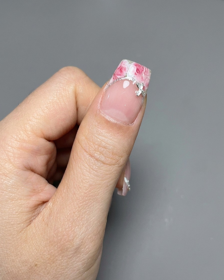 Une pince déposant un sticker de rose sur une pointe de french manucurée.