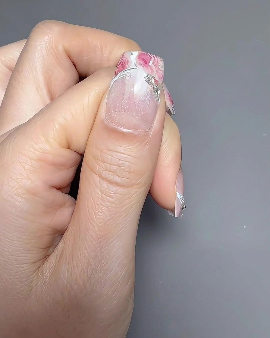 Un pinceau appliquant une couche de top coat brillant sur un ongle décoré.