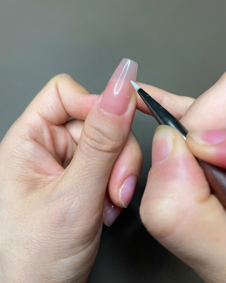 Gros plan dun pinceau liner appliquant du gel blanc pour former des pétales sur un ongle nu.